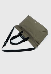 Sac fourre-tout vert olive en tissu durable, avec des poignées noires, une fermeture éclair et un logo minimaliste à l'avant. Texture lisse.