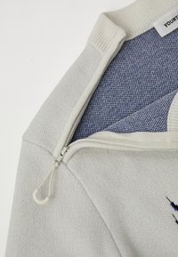 Ανοιχτό γκρι φούτερ με υφασμάτινη επιφάνεια, που διαθέτει σχέδιο μισού φερμουάρ, λευκό ριμπ απο collar και μπλε υφασμάτινη λεπτομέρεια στο εσωτερικό.