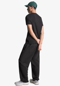 Tricou negru cu mânecă scurtă, asociat cu pantaloni negri largi. Pantofi sport gri cu talpă din cauciuc și o șapcă verde. Siluetă simplă și relaxată.