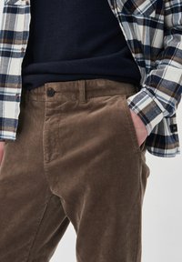 Braune Cordhosen mit verticalen Rippungen, kombiniert mit einem karierten Hemd in Blau, Weiß und Braun. Verfügt über einen Knopfverschluss und seitliche Taschen.