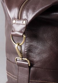 Brown leather bag featuring a zipper, gold hardware, and a clip attachment. Textured surface with visible stitching details.