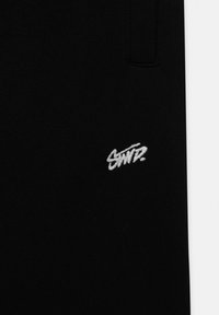 Black fabric sweatpants with a close-up view of a white embroidered logo "SNTZ" positioned on the left side. Soft texture, elastic waistband.