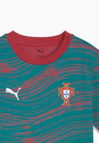 Grünes und rotes Portugal-Fußballtrikot mit rotem Kragen, wellenförmigen roten Streifen, Puma-Logo und Wappen des Portugiesischen Fußballverbandes auf der Brust.
