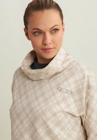 Felpa leggera beige con collo a cowl e motivo geometrico, dotata di un logo in pietre brillanti sul petto. Texture liscia, vestibilità comoda.