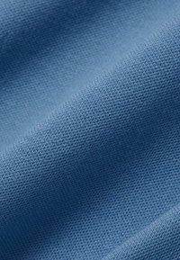 Close-up van zacht, lichtblauw gebreid stof met fijne textuur en subtiele vouwen of draperingseffect.