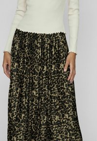Plisseret nederdel med et sort og beige leopardprintdesign, parret med en cremet ribbet top med bølgede manchetter.