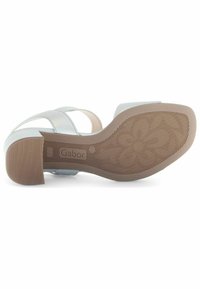 Sandal in argento con cinturini incrociati, tacco basso a blocco e suola in gomma testurizzata. Presenta un colore chiaro e il logo del marchio sulla suola.