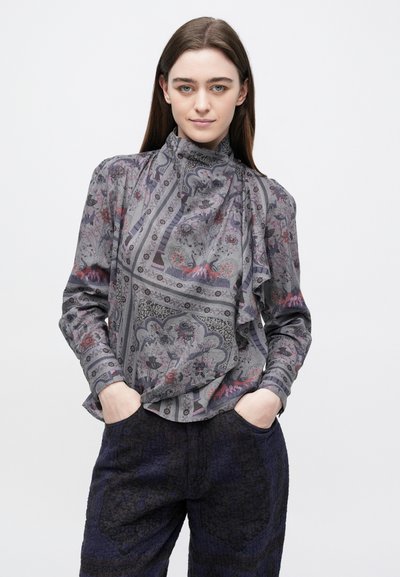 Γκρι μπλούζα με σχέδιο σε πατρόν και λαιμόκοψη με βολάν, διακοσμημένη με περίπλοκα λουλουδένια και γεωμετρικά μοτίβα σε διακριτικά χρώματα. Συνδυάζεται με υφασμάτινο σκοτεινό παντελόνι.