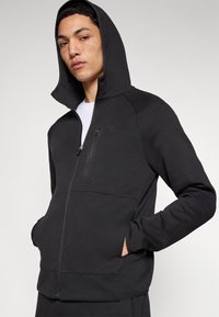 Felpa nera con zip, ampio cappuccio, tasche frontali e una tasca sul petto con zip. Realizzata in tessuto strutturato, con logo.