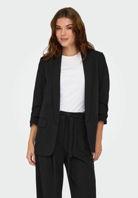 Sort skræddersyet blazer med lange ærmer, opsmøgte manchetter og lapeller. Sammen med en hvid skjorte med en struktureret silhuet.