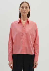Chemise boutonée rose clair avec des manches longues, un col et une poche poitrine. Fabriquée en tissu lisse, avec une coupe légèrement ample.