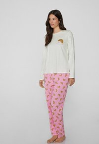 Camiseta blanca de manga larga con un gráfico de croissant y el texto "petit croissant"; pantalones rosas con un patrón de croissants marrones; tela suave, corte relajado.