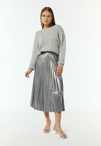 Grijze gebreide trui met een gestructureerd patroon, gecombineerd met een metallic zilveren midi rok met plissé en zilveren sandaaltjes met hak.