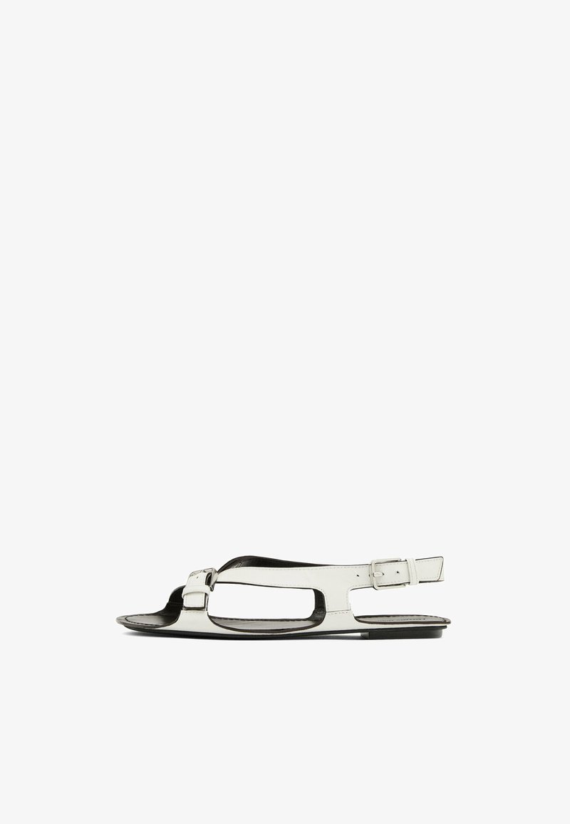 White leather sandal with a flat sole, open toe design, and side buckle strap. Features cut-out details along the sides.