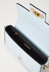 Bolso de mano de cuero azul claro con detalles en negro, cierre a presión magnético, forro de tela negra, bolsillo interior con cremallera y diseño estructurado.