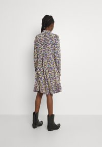 Blumenkleid mit langen Ärmeln, mehrfarbiges Blumenmuster auf schwarzem Hintergrund, A-Linien-Silhouette, geraffter Rücken, kombiniert mit schwarzen Cowboystiefeln.