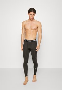 Leggings sportivi neri con un design aderente, dotati di una vita con marchio e un piccolo dettaglio del logo vicino alla caviglia. Texture liscia.