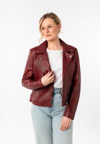 Bordeaux leren motorjack met zilverkleurige hardware, ritszakken en een ingesneden kraag. Gecombineerd met een witte top en licht denim.