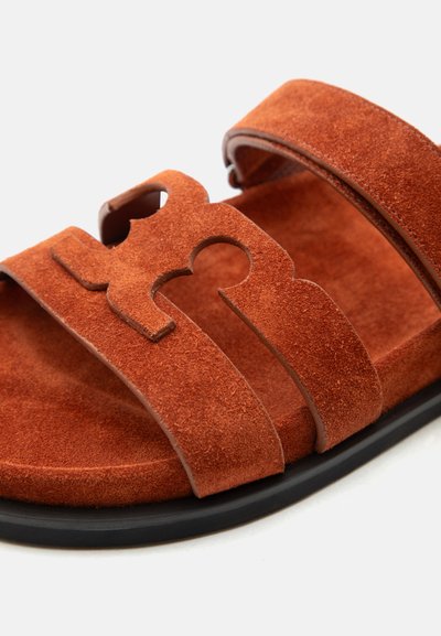 Sandale en daim marron avec double bride, un design décoratif avec découpes et une semelle en caoutchouc noire sur fond blanc.