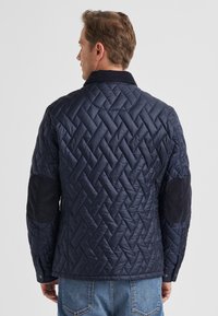 Marineblaue Steppjacke mit Diamantmuster, Kord-Ellenbogenpatches und Druckknopfverschluss. Glattes, leichtes Material.