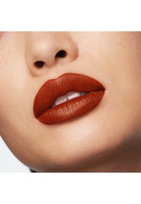 Rouge à lèvres mat, terracotta profond sur des lèvres pulpeuses, mettant en valeur la texture lisse et les contours définis sur un teint clair.