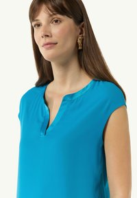 Türkise Bluse mit V-Ausschnitt und kurzen Ärmeln, gefertigt aus glattem Stoff. Verfügt über einen glänzenden Besatz am Ausschnitt für zusätzliche Details.