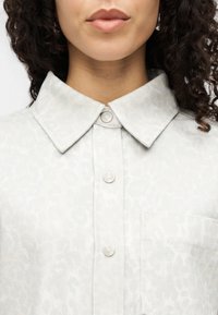 Πουκάμισο με λεοπάρ τύπωμα σε ανοιχτό γκρι, με μυτερό γιακά, πέντε κουμπιά μπροστά και μία τσέπη στο αριστερό στήθος.