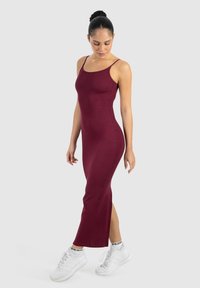 Burgunderfarbenes Midikleid mit Spaghetti-Trägern, gerippter Textur, figurbetonter Passform und Seitenschlitz; kombiniert mit weißen Sportschuhen.