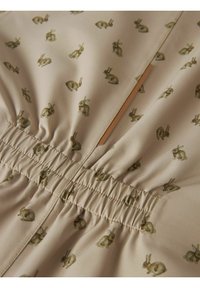 Tejido beige con un patrón de conejos repetido, con goma fruncida en la cintura y una textura de superficie suave.