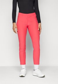 Pink stretch trousers with a slim fit, featuring a front button closure and ankle zippers, paired with white sneakers and socks.