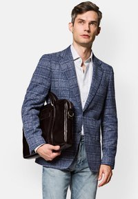 Niebieska marynarka w kratę, jasna koszula i wyblakłe dżinsy noszone przez modela trzymającego ciemnobrązową skórzaną torbę. Zauważalne detale w tkaninie i designie.