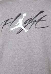 Silhouette blanche d'un joueur de basketball sautant avec un bras tendu au-dessus du texte noir stylisé "Flight" sur fond de tissu gris.