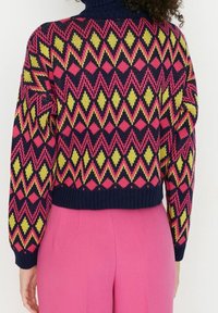 Sweter dziany z geometrycznym wzorem w różowe, żółte i granatowe kolory, z wysokim kołnierzem i prążkowanym obszyciem. Krótkie krojenie z teksturowaną tkaniną.