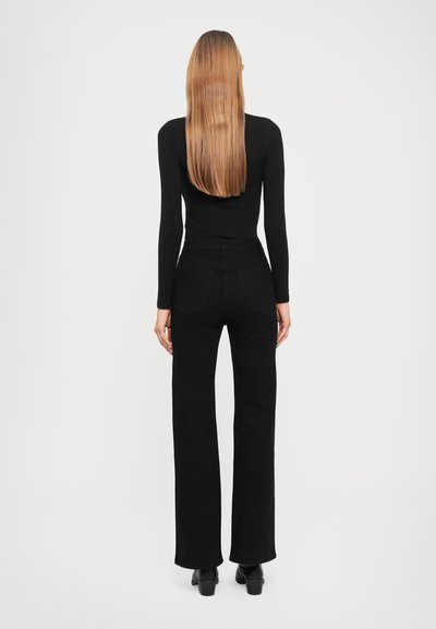Black long-sleeve top paired with high-waisted black pants, featuring a straight cut and two back pockets. Model facing away, hair cascading down.