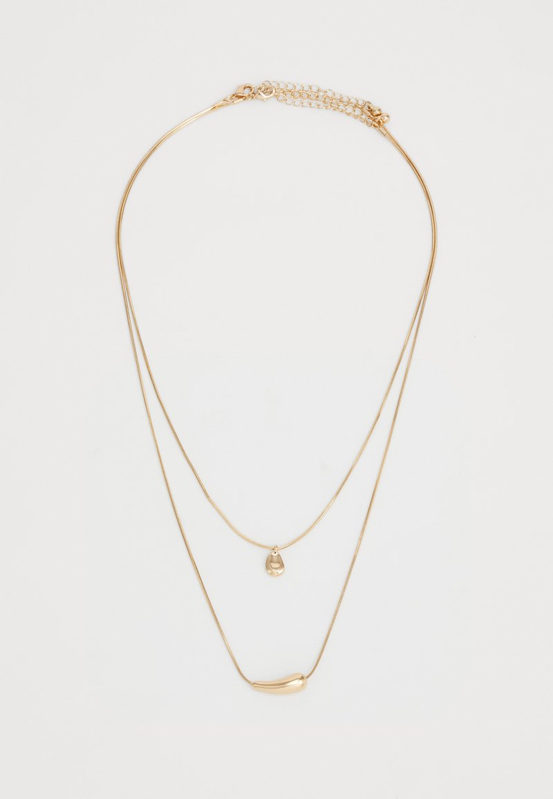 Divkārši zeltīti kaklarota ar divām gludām, neregulārām formām uz plānām ķēdēm uz vienkārša balta fona.