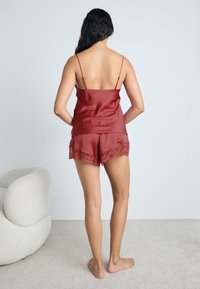 Ensemble en satin rouge comprenant un camisole et un short avec des bordures en dentelle, des bretelles réglables et une coupe ajustée. Texture lisse sur le haut et le short.