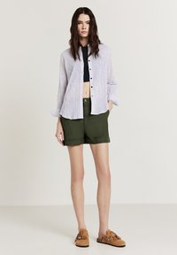 Gestreifte button-up Hemd, verkürztes schwarzes Tanktop, olivgrüne Shorts und braune Wildleder Schlupfschuhe mit Fransen.
