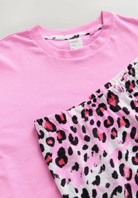 Roze katoenen T-shirt met een onderste paneel met luipaardprint, voorzien van zwarte en roze vlekken. De elastische tailleband is zichtbaar op de bedrukte stof.
