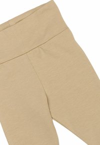 Bež legice s širokim, rebrastim pasom, z mehko, gladko teksturo in obliko, ki se prilega telesu. Vidni so šivi.