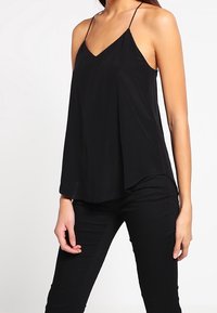 Svart ärmlös topp med V-ringning, gjord av lättviktsmaterial. Har tunna axelband och en luftig design med en något rundad kant.