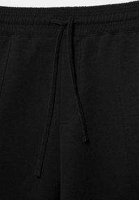 Sorte joggingbukser med elastisk taljebånd og synlig snor bundet i en knude foran i midten.