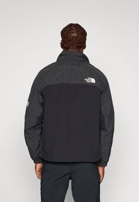 Jachetă puffer neagră cu o secțiune superioară texturată de culoare gri și o secțiune inferioară neagră solidă, având logo-ul North Face pe spate și pe manșete.