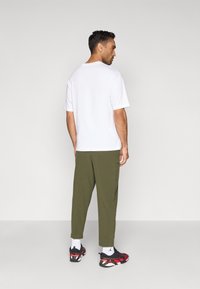 Λευκό κοντομάνικο μπλουζάκι με στρογγυλή λαιμόκοψη συνδυασμένο με ελαιδί παντελόνι με στενή κόψη και μαύρα και κόκκινα αθλητικά παπούτσια. Μινιμαλιστικός σχεδιασμός.