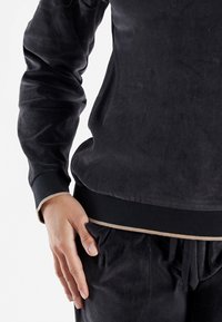 Sweatshirt in velluto nero con maniche lunghe e polsini a coste. Caratterizzato da una vestibilità affusolata e un bordo beige a contrasto all'orlo.