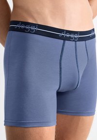 Boxers de color azul claro, hechos de una tela suave, con una cinturilla de color marino que presenta una marca blanca y costuras planas para un acabado suave.