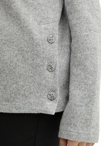 Grå, texturerad cardigan med tre knappar, tyget är mjukt och något fluffigt. Manschetten är bred med en ren finish.