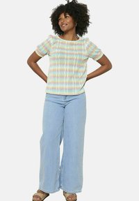 Top corto a maniche corte con motivo a zigzag multicolore e una vestibilità comoda, abbinato a jeans a gamba larga di un blu chiaro e sandali abbelliti di colore beige.