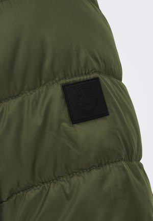 Zöld steppelt dzseki sima textúrával és fekete szövetcímkével, amelyen dombornyomott logó részlet található. A design könnyű és laza.