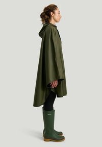 Vihreä vedenpitävä sadeponcho, joka on valmistettu sileästä materiaalista ja jossa on huppu. Poncho on päällä mustien legginsien ja ruskeapohjaisten vihreiden kumisaappaiden kanssa.