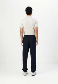 Lyse beige polo-shirt med subtile logo-detaljer og bukser med elastisk talje i marineblå. Suppleret med lyse sneakers, set fra bagenden.